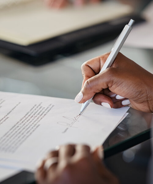 Close up of hand of a business woman signing agreement document in modern office.